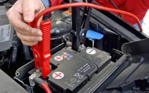 Hand befestigt rote Klemme an Autobatterie. Die richtige **Starthilfe Reihenfolge** ist entscheidend für die Sicherheit.