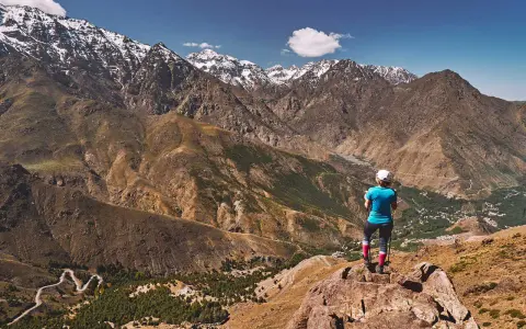 Widok na ośnieżone szczyty górskie Jebel Toubkal. Turystka podziwia panoramę z skalistego zbocza.