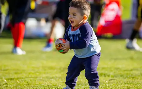 Niño feliz jugando con una pelota de fútbol americano, disfrutando de los juegos con pelotas para niños en un día soleado.