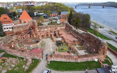 Ruiny zamku bierzgłowskiego z czerwonej cegły, z widokiem na rzekę i most.
