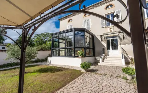 Une élégante véranda moderne s'intègre à une maison de campagne. La surface de plancher pavée mène à des marches menant à la porte d'entrée.