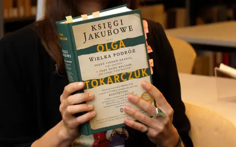 Osoba trzyma książkę "Księgi Jakubowe" Olgi Tokarczuk, z zakładkami w różnych kolorach.