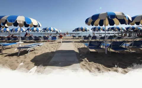Ombrelloni a righe blu e bianche e lettini preparati per i visitatori al Delfini Beach Village Cattolica, con il mare sullo sfondo.