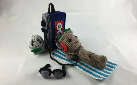 Amigurumi Baby Groot tumbado con auriculares junto a un reproductor de música y un pequeño personaje gris.