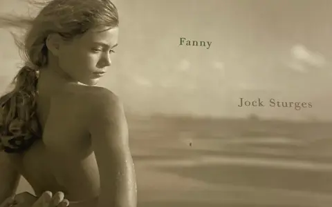 A young woman, Fanny, is captured by Jock Sturges on a beach, her hair blowing in the wind.