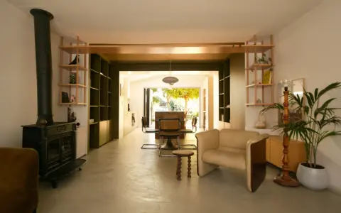 Aménagement maison en longueur : salon avec poêle, étagères et vue sur salle à manger et jardin.