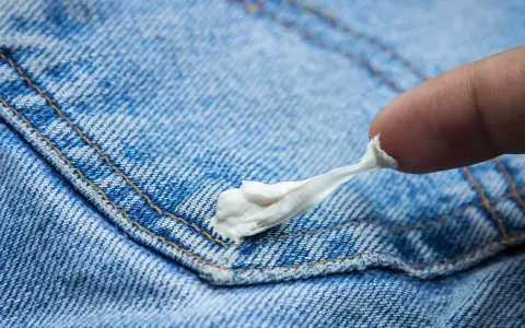 Ein Finger versucht, Kaugummi von Jeans zu entfernen. Der klebrige Kaugummi zieht sich zäh.