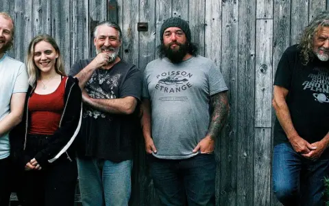Le groupe de Robert Plant, avec ses musiciens, pose devant un mur de bois.