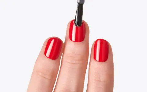 Application d'un top coat sur des ongles rouges brillants. Le top coat, c'est quoi ? C'est la touche finale pour une manucure parfaite.