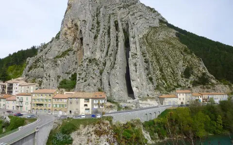 Imponerande klippformation vid Route Napoléon. En by klättrar uppför bergssluttningen, med en bro och en turkos flod nedanför.