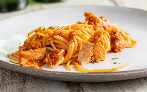 Spaghetti al tonno conditi con un sugo saporito e ricchi pezzi di tonno, guarniti con prezzemolo fresco.
