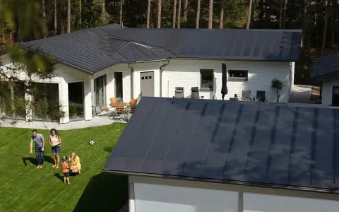 Familj njuter av solen på gräsmattan framför ett modernt hus med ett stilrent lindab solar roof.