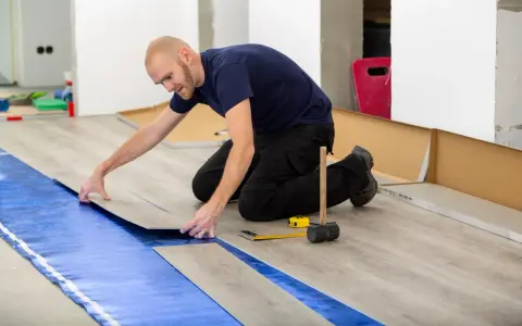 Pose d'un revêtement de sol stratifié sur une sous-couche d'isolation phonique sous carrelage. Outils de pose à proximité.