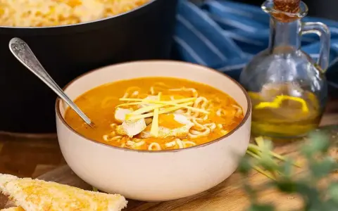 En skål med kycklingsoppa med nudlar och kycklingbitar, serverad med rostat bröd. Ett recept på kycklingsoppa som ser utsökt ut.