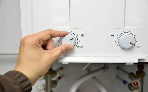 Mano girando el dial del termo eléctrico para cerrar la llave de paso.