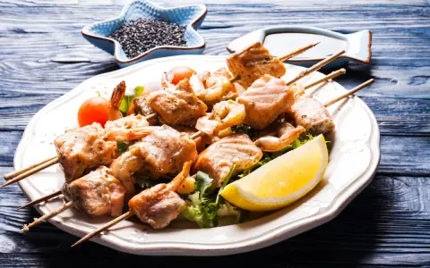 Spiedini di pesce succulenti, con gamberi e salmone grigliato, serviti su un letto di insalata con spicchio di limone.