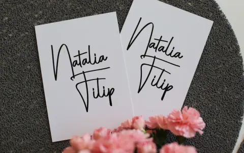 Dwie białe kartki z napisem "Natalia Filip" w ozdobnej czcionce. To piękne zasady zaproszenia na uroczystość.
