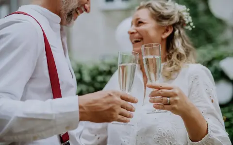Szczęśliwa para wznosi toast szampanem. To ich piękny ślub po 40. roku życia.