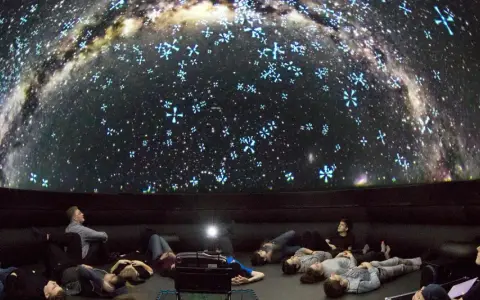 Besucher im Planetarium Berlin liegen und sitzen und blicken gebannt auf die Projektion der Milchstraße und funkelnder Sterne.