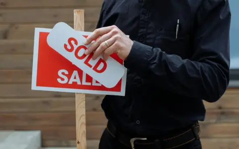 Hombre coloca cartel de "Vendido" sobre uno de "En Venta". Una venta rápida, quizás por debajo del valor de referencia.