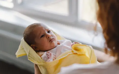 Malutki noworodek pierdzi, ale nie robi kupy. Otulony w żółty kocyk, patrzy z uwagą.
