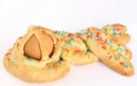 Dolci calabresi pasquali: un uovo incastonato in una treccia di pane dolce, decorata con zuccherini colorati.