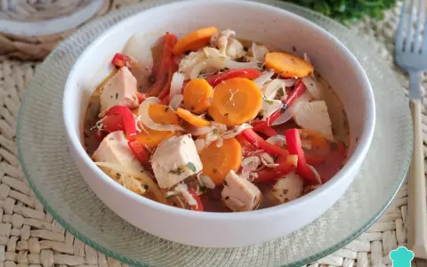 Pechuga de pollo en escabeche con zanahoria, pimiento rojo y cebolla, servida en un cuenco blanco sobre una base tejida.