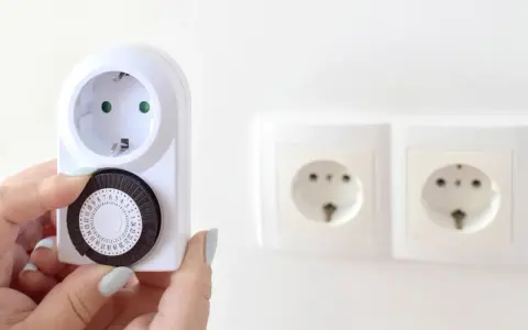 Une main ajuste le cadran d'un minuteur mécanique, montrant comment fonctionne un minuteur pour programmer des appareils électriques.