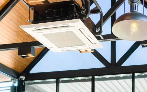 Unidad de cassette de un sistema VRV integrada en un techo de madera y metal, con luces y tuberías visibles.