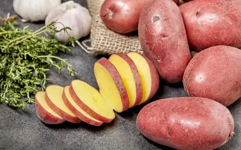 Czerwone ziemniaki, jeden pokrojony w plastry, obok czosnku i ziół.