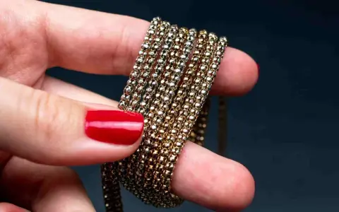 Main d'une femme aux ongles rouges tenant une chaîne de métal doré, montrant comment nettoyer métal doré noirci.