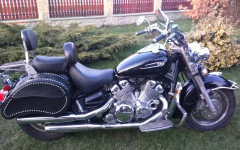 Czarny motocykl Yamaha Royal Star z chromowanymi detalami i skórzanymi sakwami, zaparkowany na trawie przed płotem.