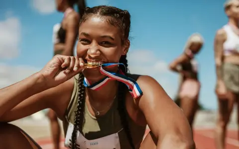 Läuferin beißt stolz in ihre Goldmedaille. Ihr Trainingsplan Laufen 10 km hat sich ausgezahlt.