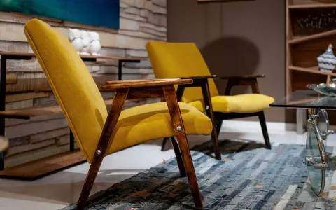 Due poltrone gialle con struttura in legno scuro, un tappeto patchwork e un tavolino in vetro. Un tocco di arredamento anni '70 italiano.