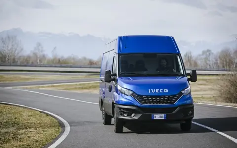 Niebieski Iveco Daily 3 na zakręcie drogi, z kierowcą za kierownicą. W tle góry i drzewa.