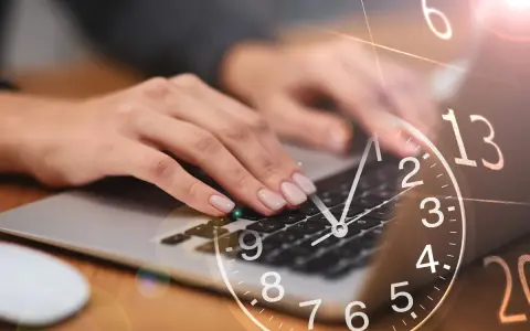 Dłonie piszą na klawiaturze laptopa, a nad nimi unosi się zegar. 0440 znaczenie czasu w pracy.