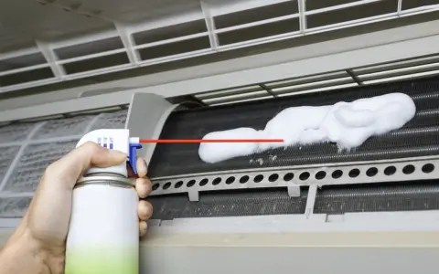 Mano rociando espuma para limpiar aire acondicionado unidad interior.