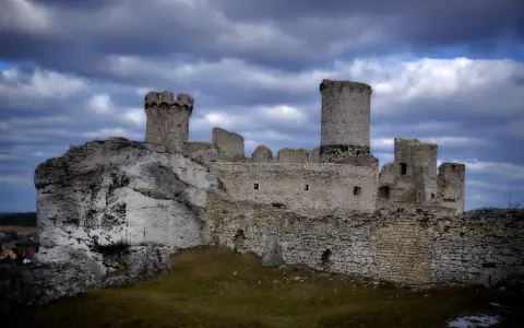 Ruiny zamku Ogrodzieniec na skale, z wieżami i murami, pod burzowym niebem. Idealne miejsce na trasę pełną historii.