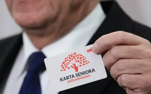 Dłoń trzyma białą kartę z czerwonym drzewem i napisem "KARTA SENIORA OGÓLNOPOLSKA".