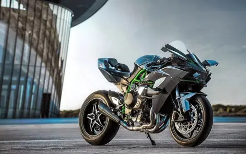Kawasaki H2R – maszyna, która w mgnieniu oka osiąga 100 km/h. Czarny, sportowy motocykl z zielonymi akcentami na ramie, zaparkowany przed nowoczesnym budynkiem.