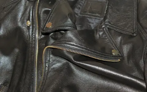 Dettaglio di una giacca in ecopelle nera con zip dorata e bottoni a pressione. Si pensa a come lavare giacca ecopelle in lavatrice.