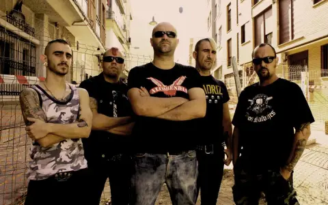 Cinco hombres con estética punk posan en una calle, listos para el rebel fest.