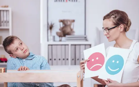 Bambino con autismo durante un test, mentre un terapista mostra faccine felici e tristi.