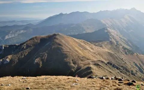 Widok na pasmo górskie Tatr. W oddali widać kolejne grzbiety górskie, a na pierwszym planie ścieżki i kamienie. Trasy Tatry zachęcają do wędrówki.