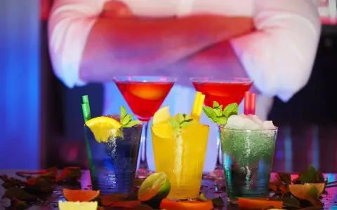 Kolorowe drinki z owocami i miętą na barze, w tle barman.