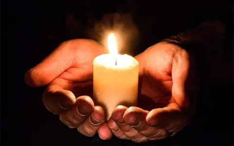 Hände umschließen eine Kerze, die ein warmes Licht spendet. Ein Symbol für evangelische Gebete und Hoffnung in der Dunkelheit.