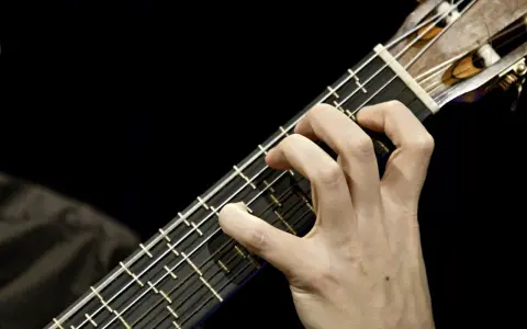 Main d'un guitariste jouant sur une microtonal guitar, ses doigts effleurant les cordes sur un manche sombre.