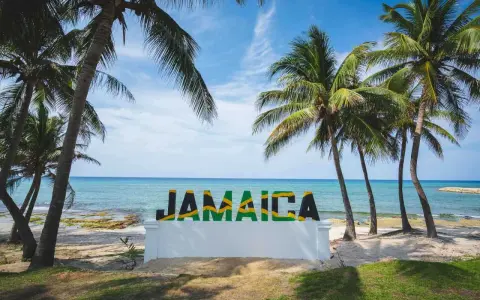 Napis "JAMAICA" na tle plaży, morza i palm.
