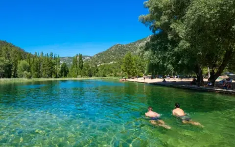 Dos hombres nadan en la cristalina piscina natural Cañamares, rodeada de vegetación y montañas.