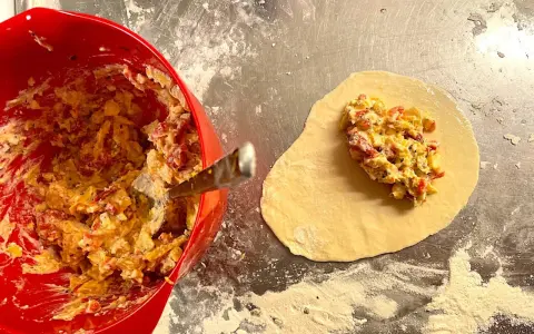 Fyllning till piroger recept läggs på deg. En röd skål med fyllning syns till vänster.